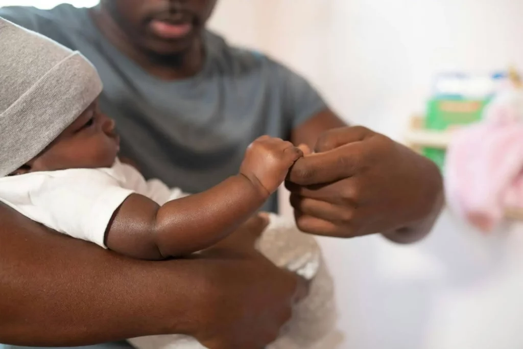 Beneficios del contacto piel con piel para el padre
Imagen de hombre con bebé en brazos, sujetándole la mano al bebé
